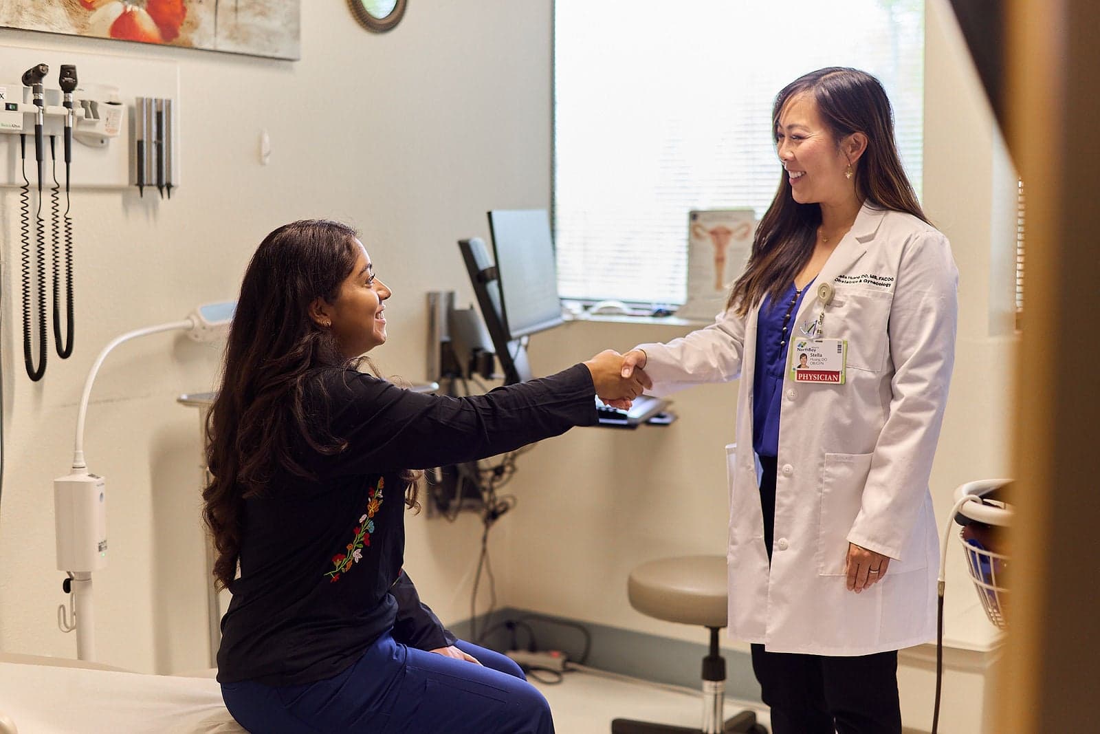 A female doctor shakes hands with a female patient in a medical clinic.