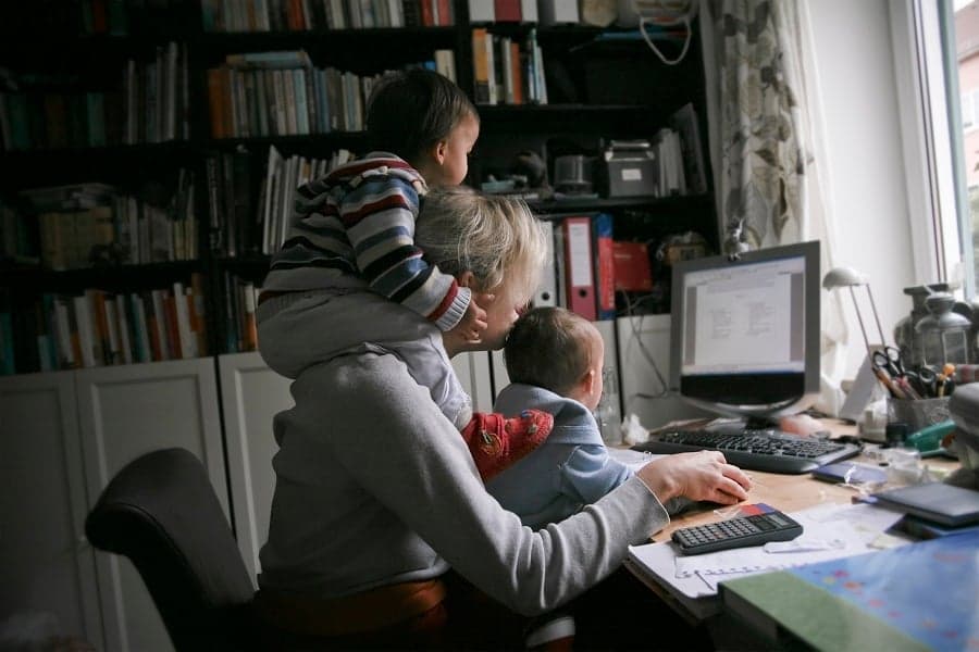 A mom looking at her computer with two kids sitting on her lap and shoulders