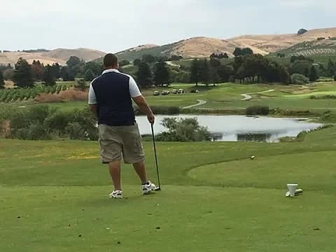 Golfer standing on green fairway preparing to putt with pond and rolling hills in background