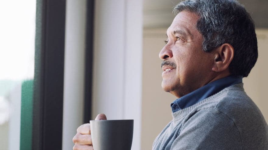 Senior man drinking coffee and looking thoughtfully out of a window.