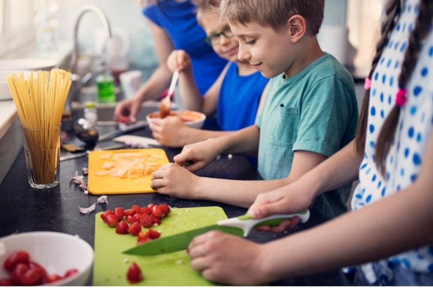 Kids being watched through how to prepare lunch by an attentive adult helper.
