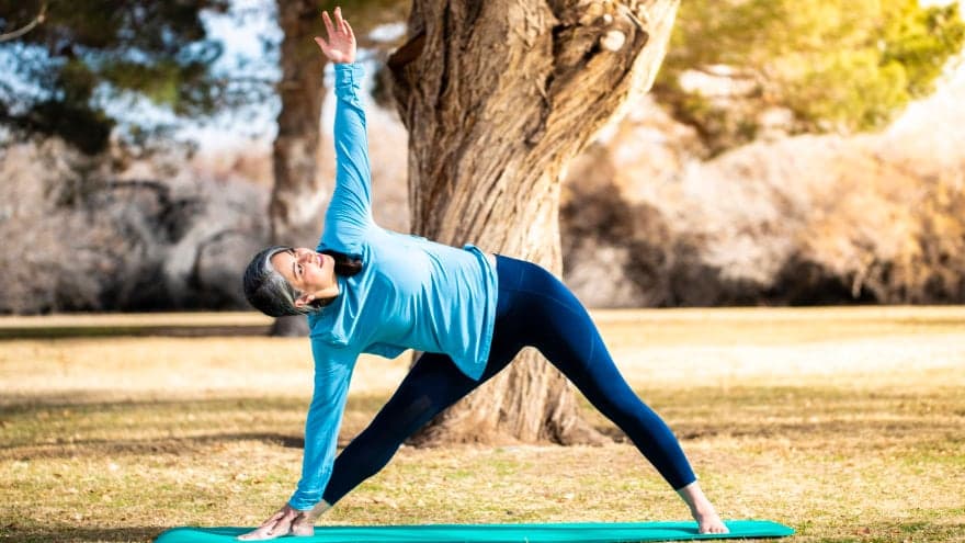 A woman doing yoga on a yoga mat in a park.