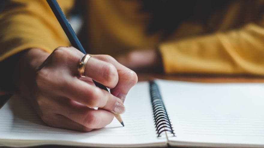 A woman’s hand preparing to write on an opened notebook.