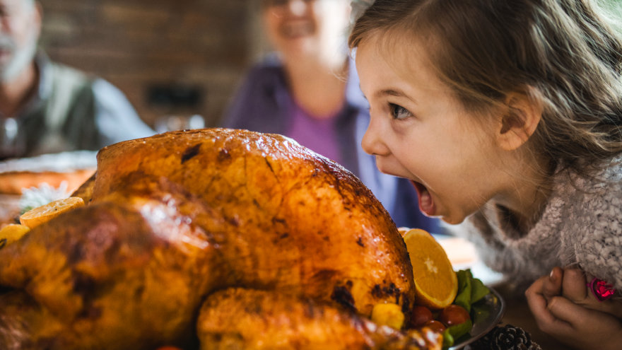 A child humorously pretends to take a giant bite out of the roasted family turkey.