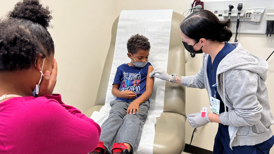 A small child receives his first COVID-19 vaccine dose at his doctor’s office.