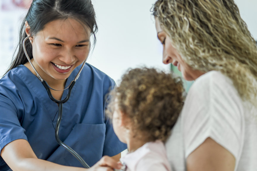 Primary care doctor smiling and examining her young patient with their mother.