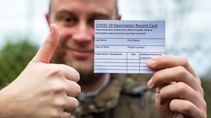 Relieved and smiling man holding up his vaccine card and giving a thumbs up.