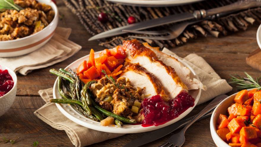 A generously packed plate on Thanksgivings featuring turkey, roasted carrots, roasted green beans, stuffing and cranberry sauce.