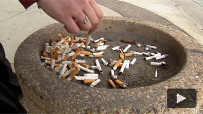 A man putting out his cigarette in a public ash tray.