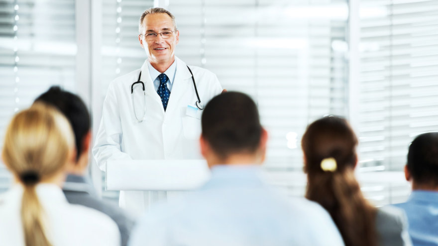 A photo of a male doctor standing in front of a crowd at a podium.