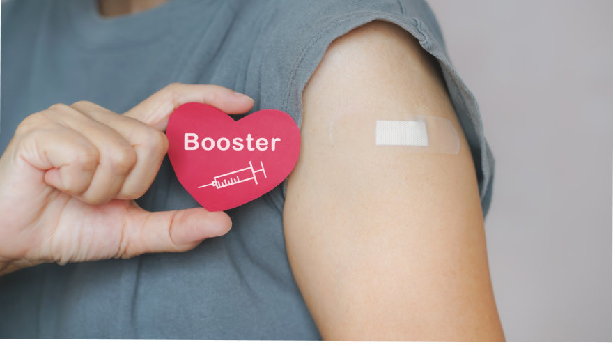 A person with a small bandage on their arm holding up a "booster" sticker.