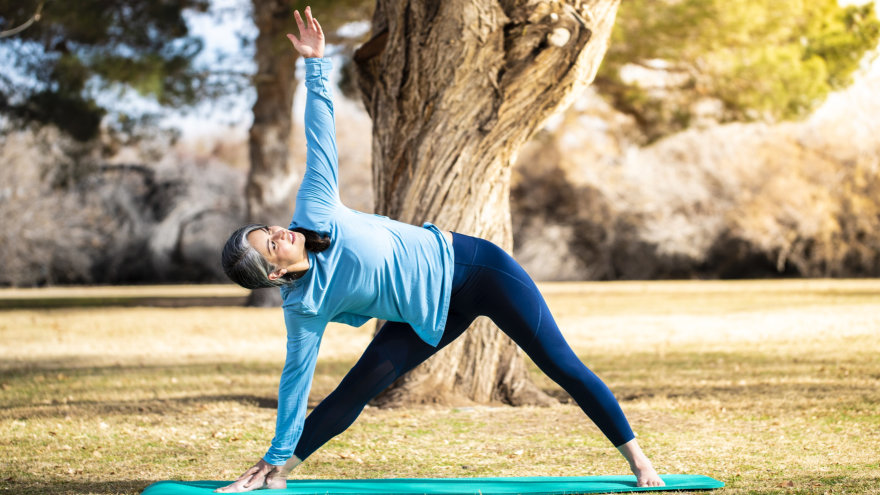 A woman doing yoga on a yoga mat in a park.