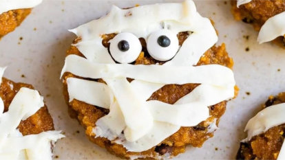 Flat, round pumpkin cookies with edible eyes and creative piped frosting to look like a mummy.