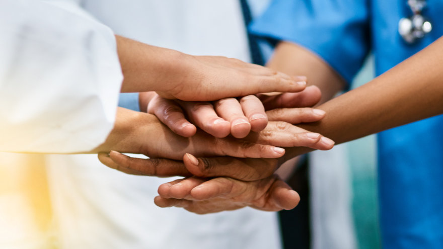 A group of doctors with their hands over each other's in the center in a symbol of camaraderie.