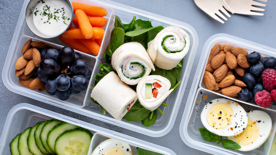 Three plastic lunch boxes with three compartments featuring variety of prepped snack like berries and nuts, carrots with ranch, hard-boiled eggs, and deli rolls.