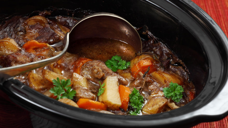 Close up of Irish stew where chunks of browned meat and thick cut vegetables can be seen. A soup ladle cuts through the middle, showing it's rich broth.
