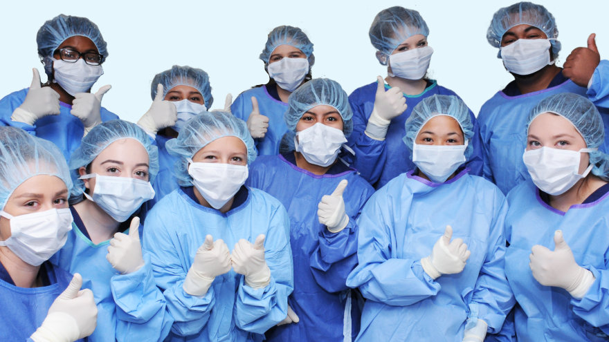 Group of previous Nurse Camp students dressed in surgical scrubs giving the camera a thumbs up.