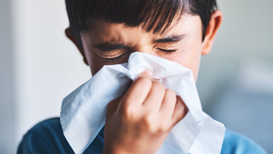 Young boy sneezing into a facial tissue.