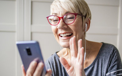 An older woman smiling and waving while on a video call on her phone.