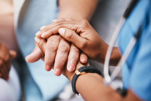 A healthcare worker warmly holding the hand of her patient. 
