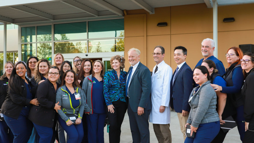 Providers and other care team members posing together with Heidi Y Campini in front of the Cancer Center entrance.